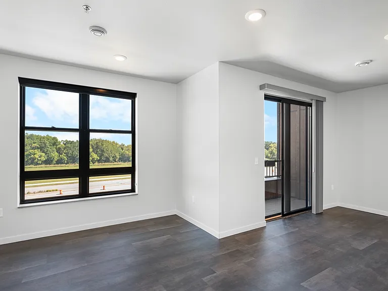Bright modern room with large windows and balcony access, featuring sleek wood flooring and neutral walls. Bright modern room with large windows and balcony access, featuring sleek wood flooring and neutral walls.