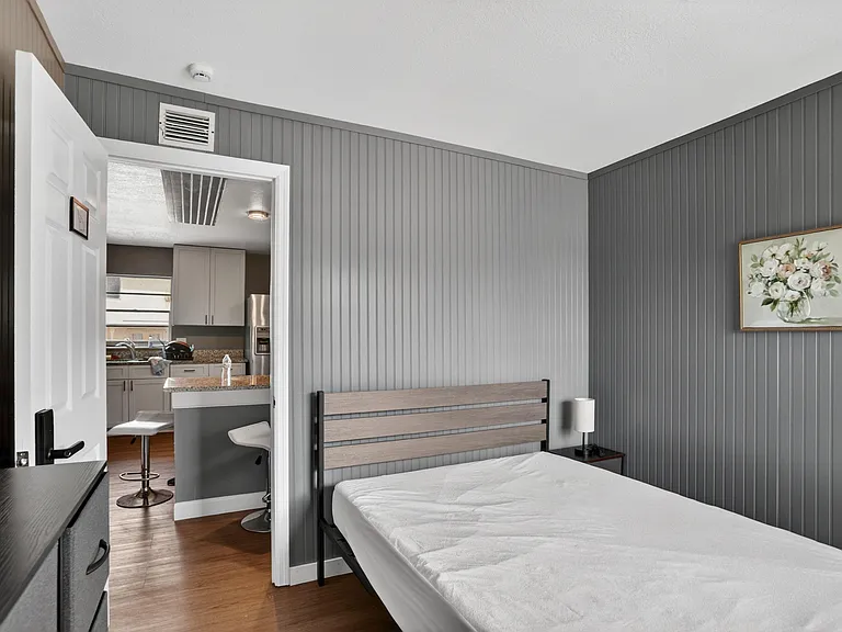 Private bedroom with paneled accent walls, space for a full/queen bed, and convenient access to the nearby kitchen.