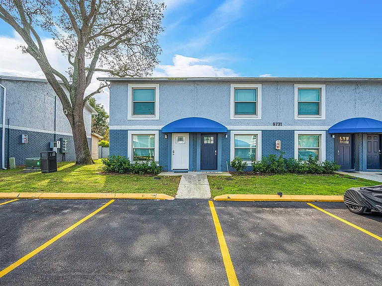 Charming two-story townhouse with modern blue exterior, featuring dual entrances and lush green surroundings.