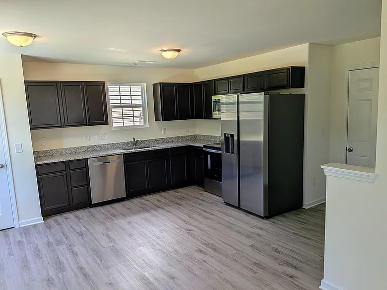 Spacious kitchen with granite countertops, ample cabinet space, and a stainless-steel appliance package featuring a double-door refrigerator.