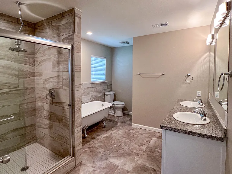Gorgeous updated primary bath with dual sinks, a clawfoot soaking tub, and a separate tiled walk-in shower.