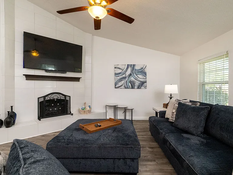 Open and inviting living room featuring a cozy couch, oversized ottoman, ceiling fan for added comfort, flat-screen Roku TV, and a beautiful indoor fireplace that adds both warmth and character.