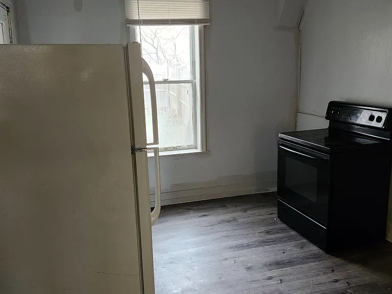 Functional kitchen space with full-size refrigerator and range, plus a window for natural light and durable flooring.