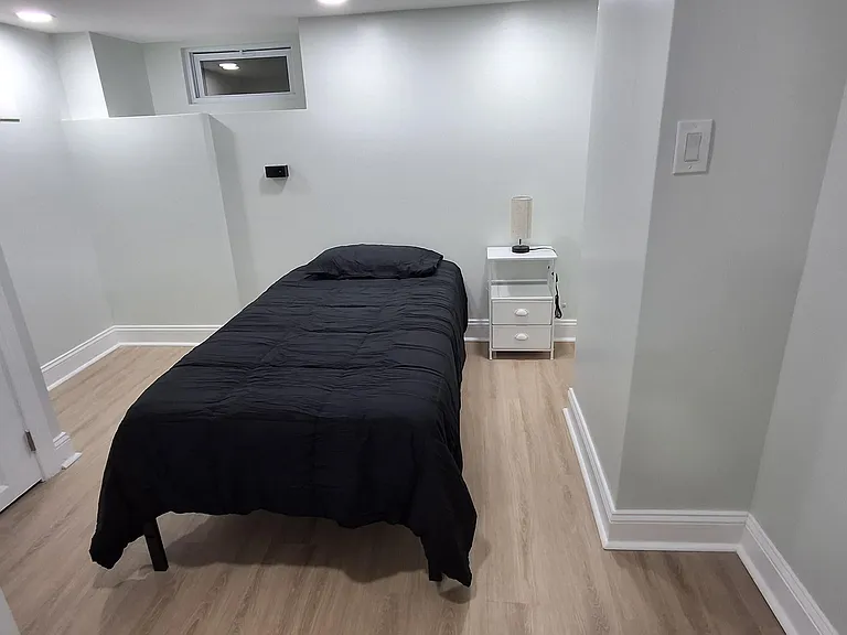 Private bedroom with wood-look flooring, overhead lighting, and a nightstand; space fits a full-size bed comfortably.
