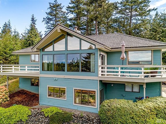View of the back of the home -- upper level from the left is bedroom, living room, and dining room.  Lower level is bedroom, two windows in the office, and the garage window.  Decks flank both sides of the living room, and the south deck wraps around to the front of the home. 