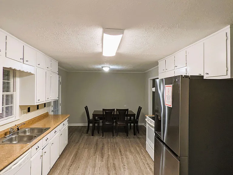 Galley kitchen with ample white cabinetry, generous counters, double-basin sink, and stainless fridge, plus space for dining.