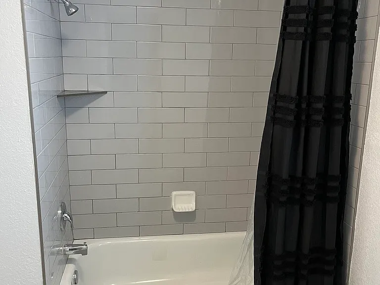 Newly renovated bath displaying new tile with curved shower curtain rod.