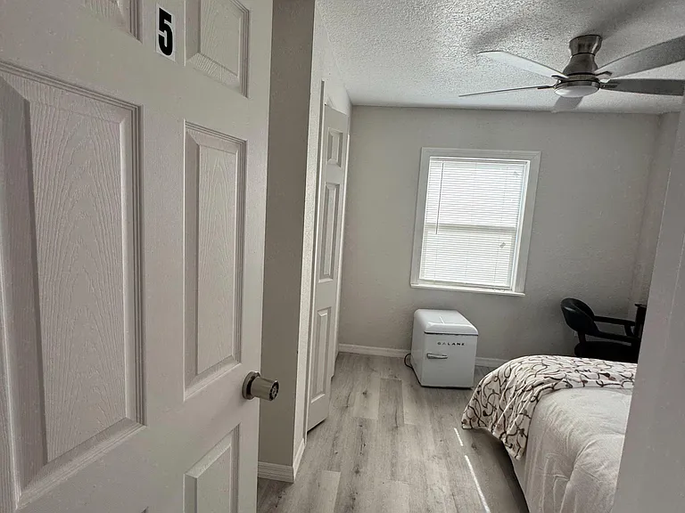 Private bedroom with a ceiling fan, window with blinds, and durable wood-look flooring; includes space for a desk setup.