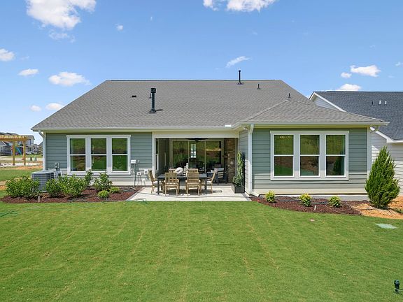 A well-manicured lawn surrounds a charming green-colored house with a covered patio, set against a b