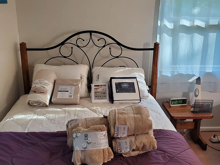 Furnished bedroom with a full-size bed, bedside table, and window with blinds for natural light and privacy.