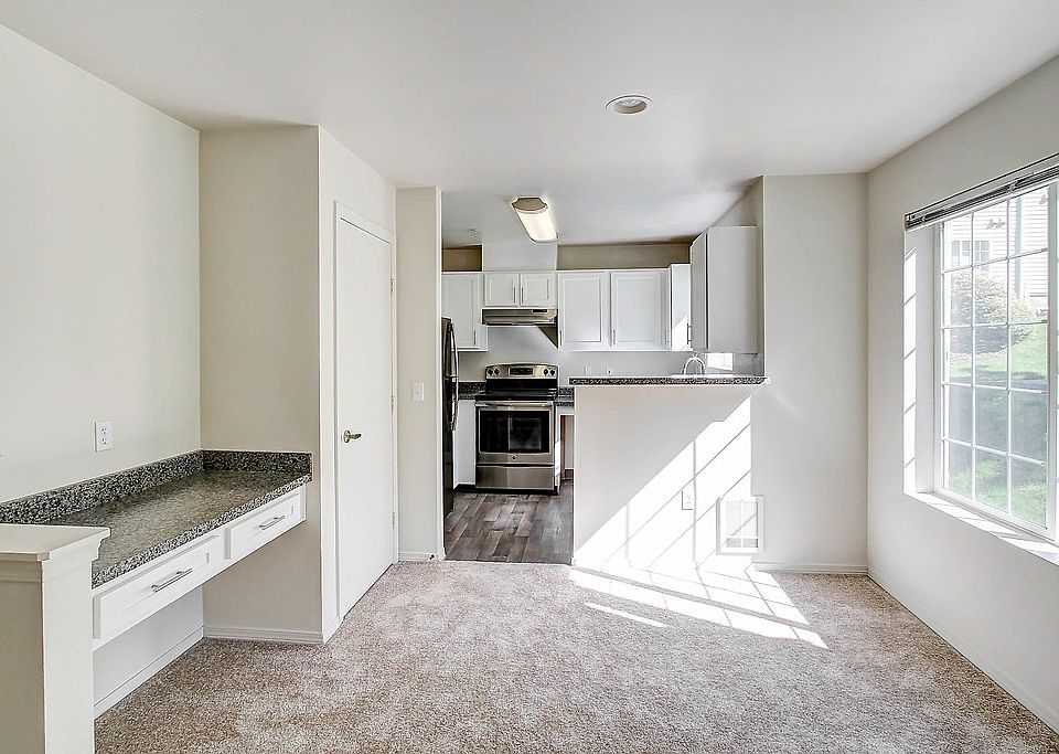 Carpeted living room with large window. Kitchen with hardwood style flooring and stainless steel appliances.