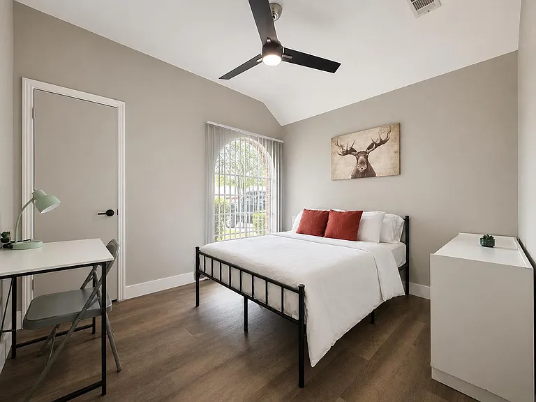 Private bedroom with vaulted ceiling, ceiling fan, arched window, and space for a bed plus desk and dresser.