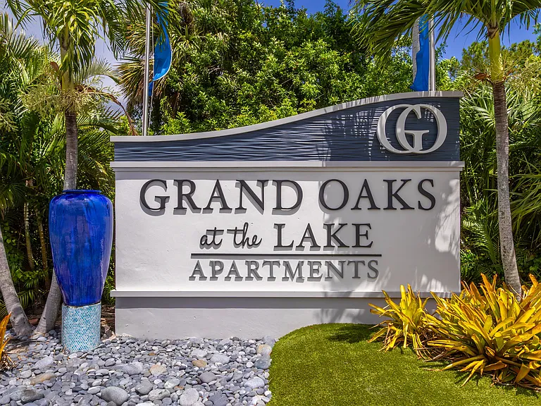 Experience the charm of Grand Oaks at the Lake Apartments, where a beautiful entrance framed by tropical landscaping sets the stage for resort-style living.