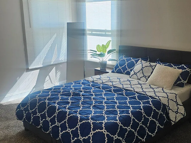 Bedroom with a queen bed, carpeted floors, and two windows with blinds for natural light and privacy.