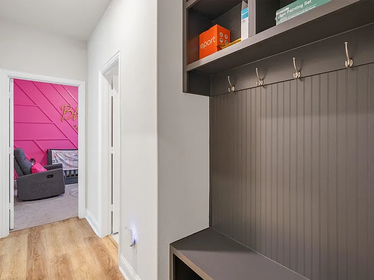 Hallway featuring wood-finish flooring, white baseboards, and a built-in storage bench with beadboard paneling and coat hooks