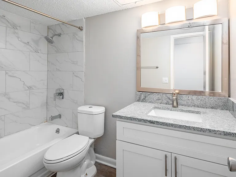 Bright bathroom with granite counters and bathtub with marble backsplash