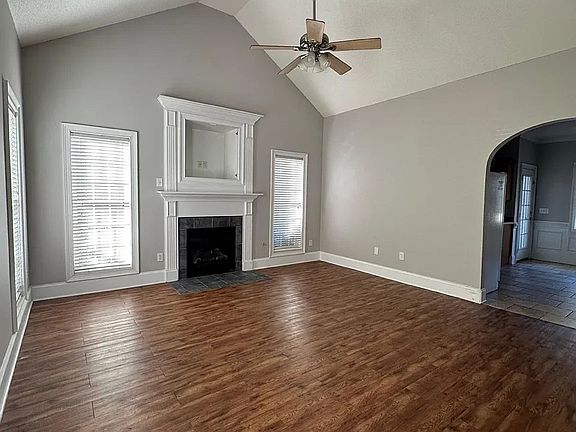 Living room, gas logs fireplace with a framed media nook above, vaulted ceiling with ceiling fan, and arched entryway to the kitchen