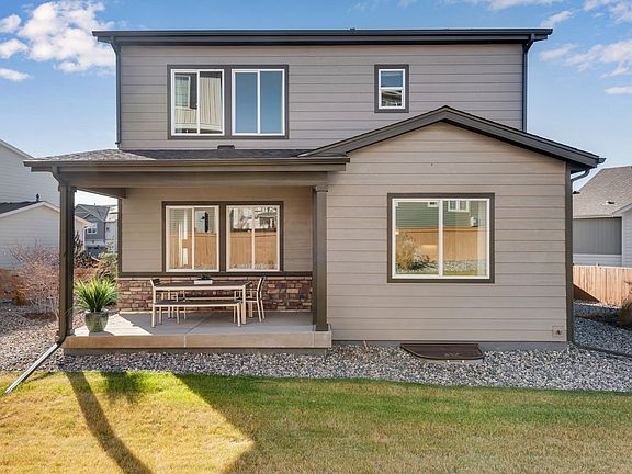 A two-story residential house with a gray exterior, a porch, and a gravel driveway surrounded by a g