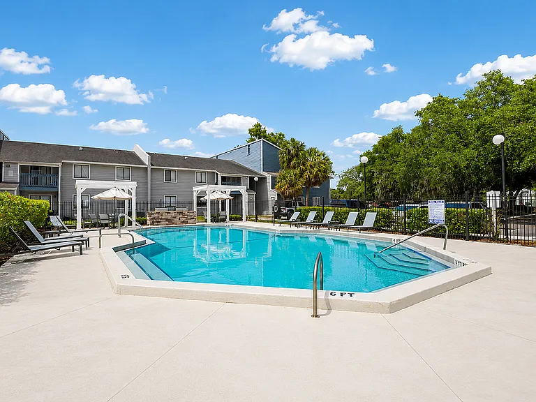 Inviting residential pool area with modern sun loungers and lush landscaping under a bright blue sky, perfect for relaxation and leisurely swims.
