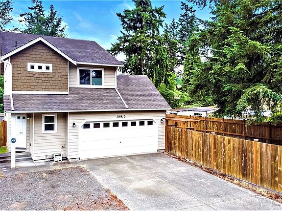 Front view of home showing front door on the side, gravel parking next to long concrete driveway & 6' wood fence wrapping around side & back yard!