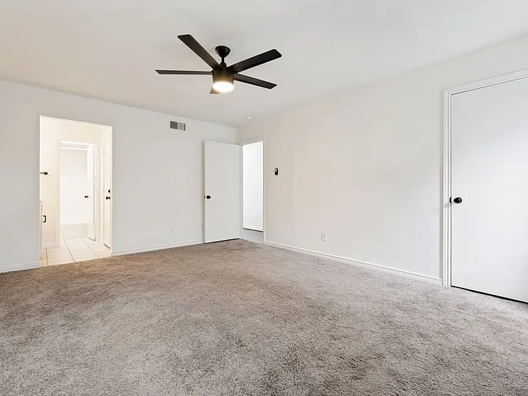 Spacious room featuring neutral carpeting and white walls, complete with a contemporary ceiling fan and light fixture