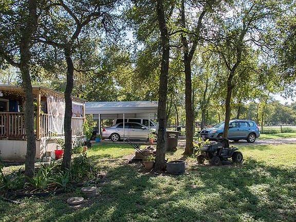 Front yard with many nice trees and a carport. Notice the covered front porch.