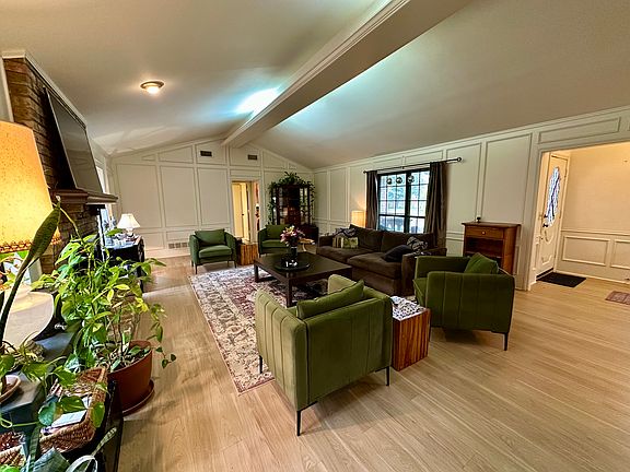 Living room with vaulted ceiling with beams, light wood finished floors, and a decorative wall