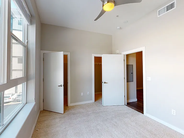 Spacious apartment bedroom with large closet, attached bathroom and plush carpet flooring.