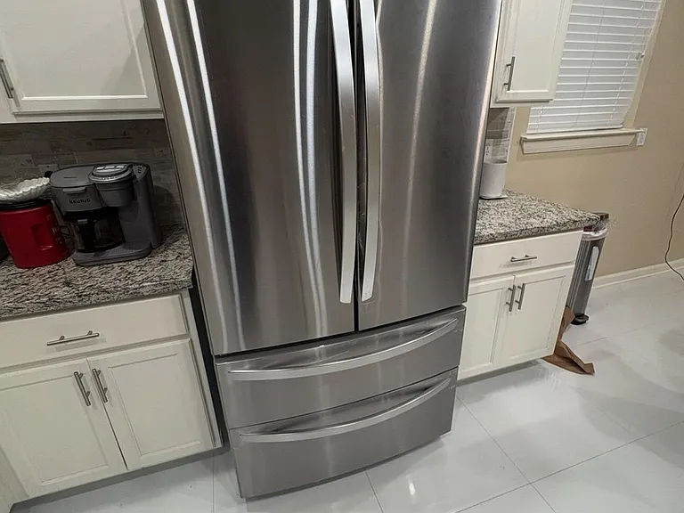Kitchen features a stainless-steel French-door refrigerator, ample white cabinetry, and granite counters for everyday meal pr
