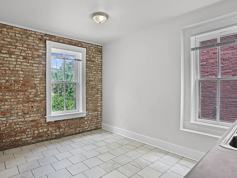 Character-filled kitchen with exposed brick, tile flooring, large windows, and space for dining.