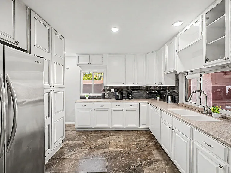 Spacious U-shaped kitchen with ample white cabinetry, generous counters, stainless fridge, dishwasher, and windowed sink.