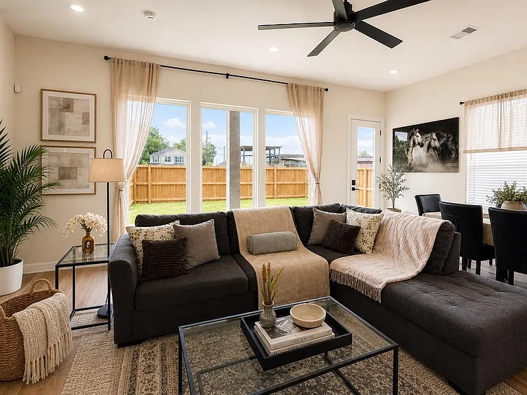Open living area with sectional seating, ceiling fan, and large windows plus a back door leading to the fenced yard.
