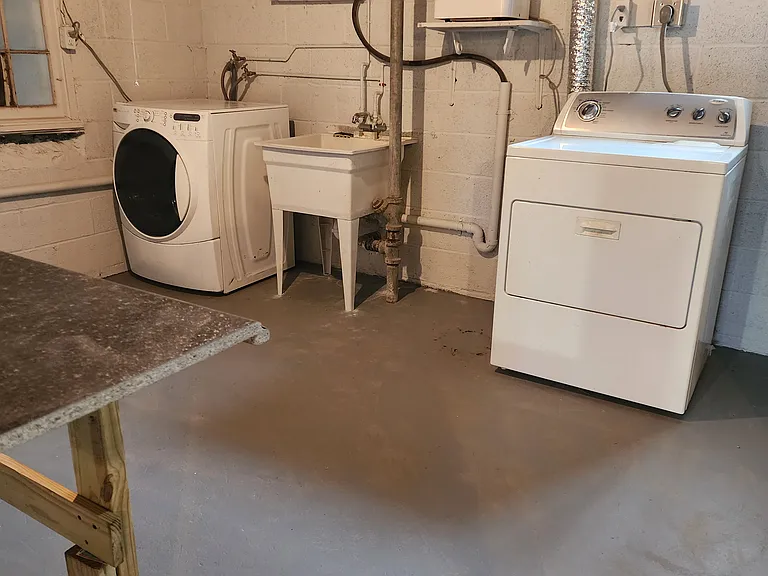 Shared laundry facility with washer and dryer, utility sink, and folding table.