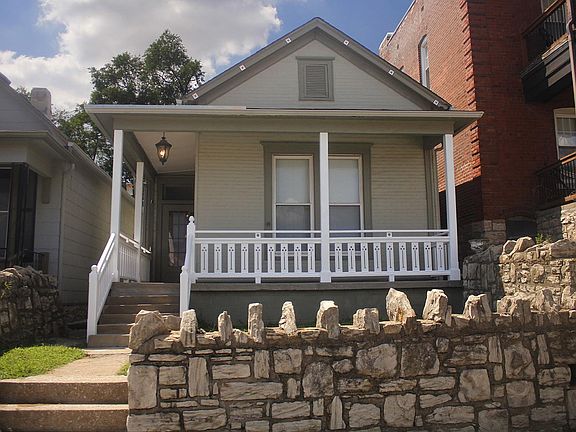 Front view with ornate porch and surrounding stone walls