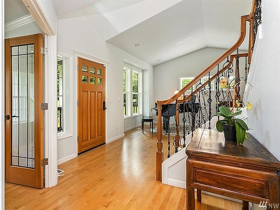 Inviting entryway with vaulted ceilings, large windows, and wood floors extending throughout home. 