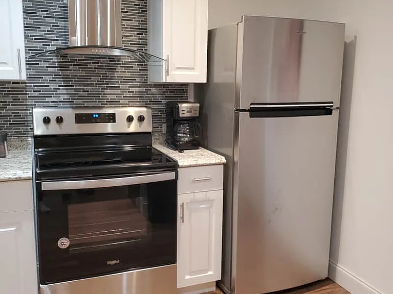 Bright and fully equipped kitchen with oven, range hood, coffee maker, and refrigerator.