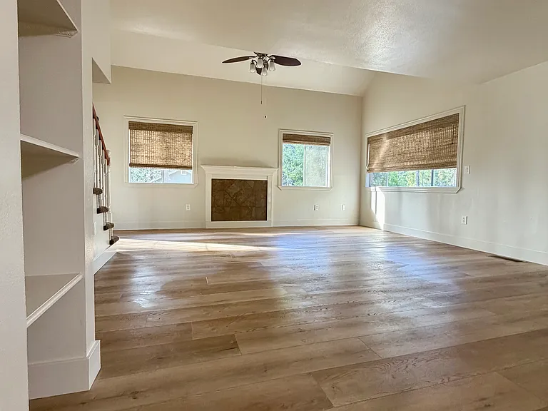 Well-lit dining and living area with ceiling fan, shelving, and sliding door out to deck