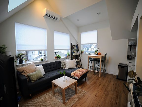 Living room is furnished with TV stand, couch, coffee table and dining table with two chairs. Lots of natural light
