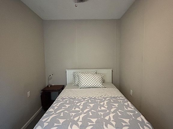 Private bedroom with a twin bed, ceiling fan, and bedside table, offering a simple layout for restful sleep.