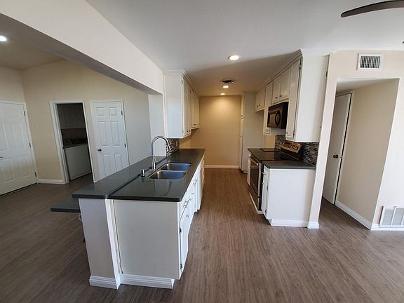 Galley kitchen with electric stove, granite counters, and dishwasher
