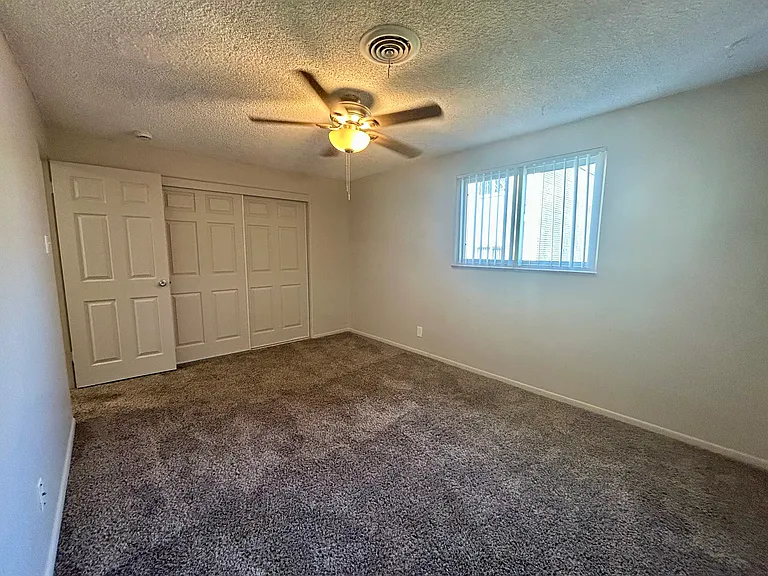 Bright and spacious bedroom with plush carpeting, featuring a ceiling fan and ample closet space. Bright and spacious bedroom with plush carpeting, featuring a ceiling fan and ample closet space.