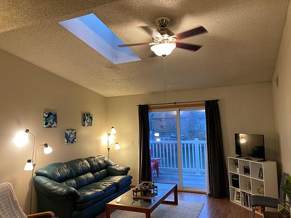 Large living room with vaulted ceiling. Balcony overlooks lake below. Skylight. Ceiling fan.