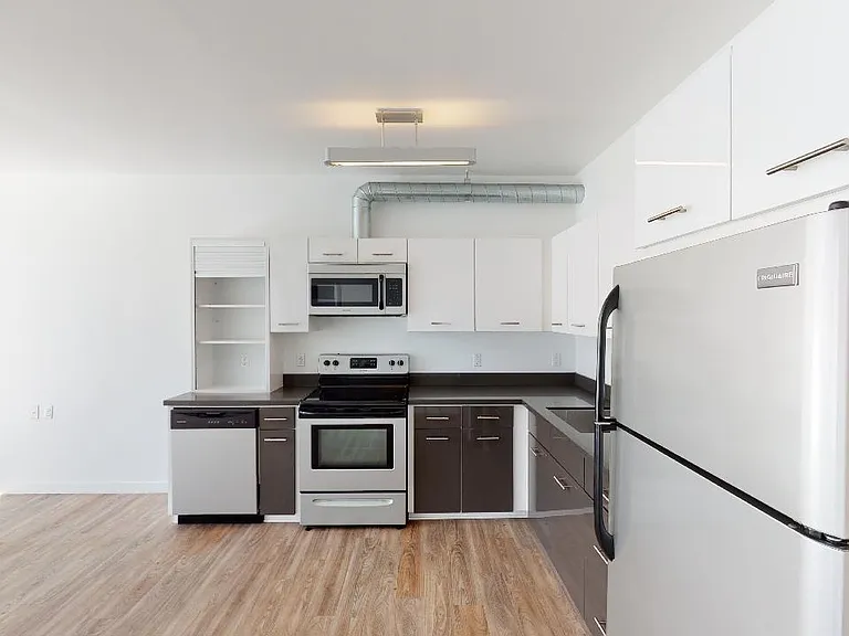 Apartment kitchen with stainless steel appliances, quartz countertops and wood-style flooring.