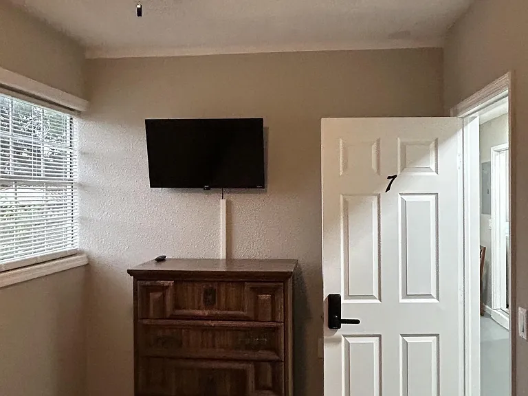 Private bedroom with window blinds for natural light, ceiling fan, and space for a dresser and wall-mounted TV.