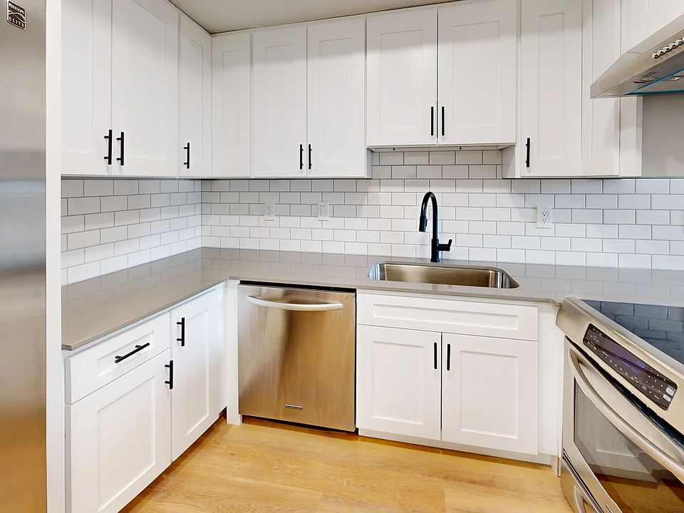White shaker cabinets, grey quartz counters, and a subway backslash adorn the kitchen.