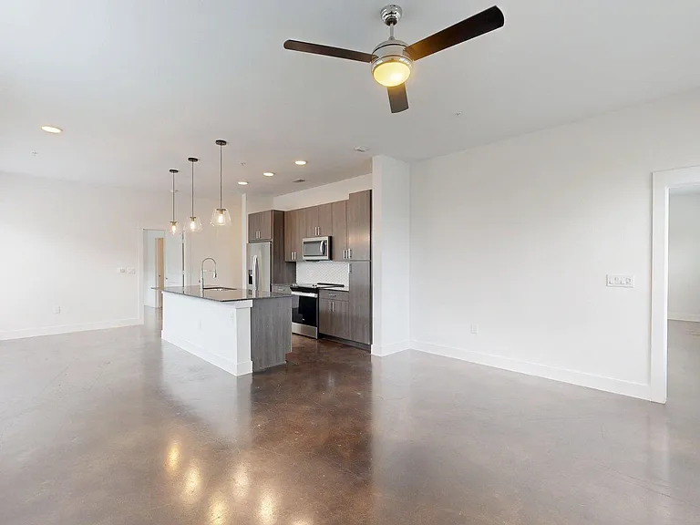 Apartment kitchen with stainless steel appliances, dining and living room with polished concrete flooring.