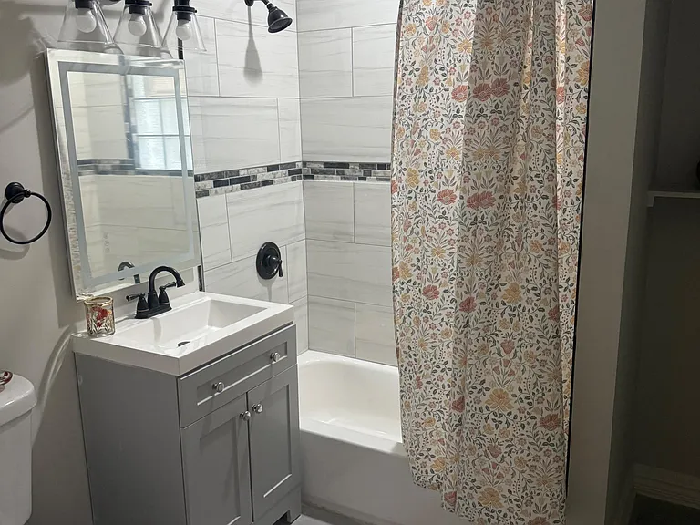 Updated bathroom with tiled tub/shower surround, single-sink vanity with storage, and modern lighting and fixtures.