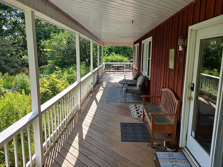 Large covered south facing porch with view of garden, lawn, and pond