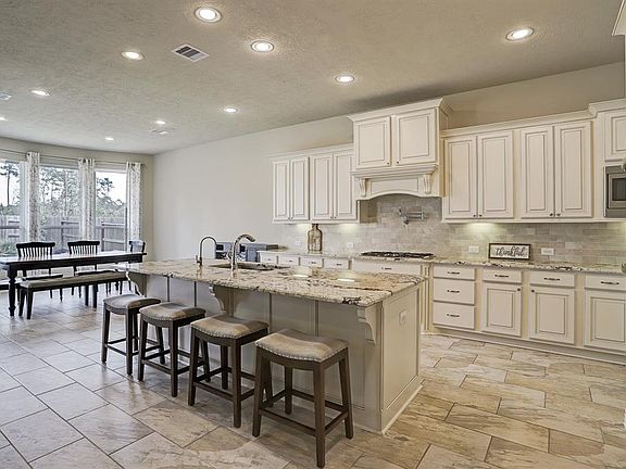 Dream kitchen featuring stainless steel appliances, large island with seating, pot filler, double ovens, 5 burner gas cooktop, under cabinet lighting and oversized tile flooring.