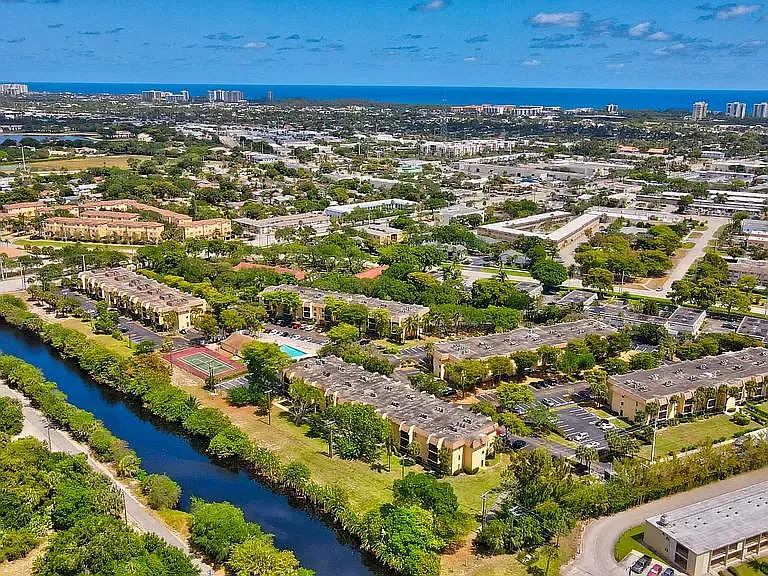 View of complex from above with unit and large banyan tree, pool, tennis courts and El Rio Canal with short distance to Boca Raton beaches and Mizner Park